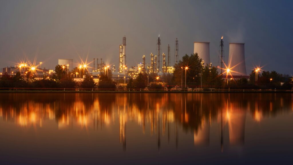 pexels photo 3105242 3105242 Industrial plant with reflection in water at twilight, showing smoke stacks and lights.