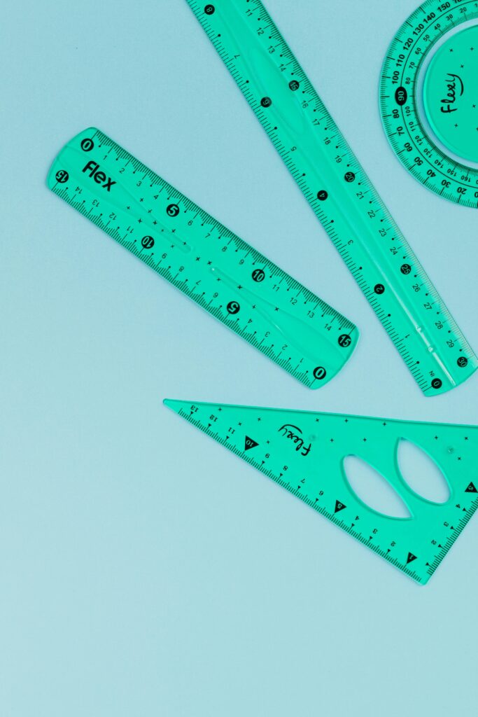 Set of turquoise measuring tools including rulers and protractor on a light surface.